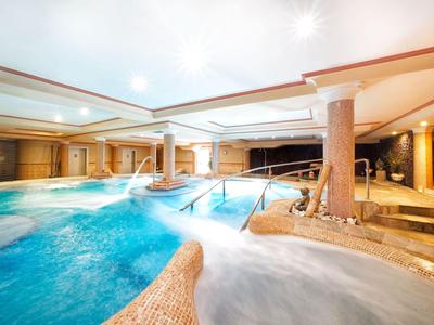 Piscina interna moderna con acqua calda, colonne e aree jacuzzi rilassanti in un ambiente alberghiero.