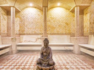 Accogliente stanza termale con piastrelle a mosaico e statua di Buddha al centro.
