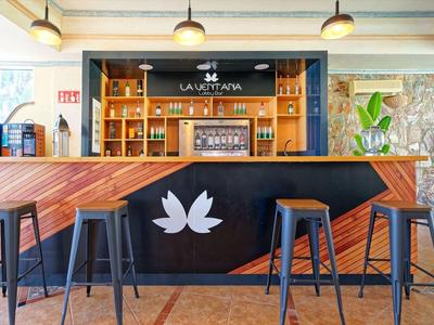 Espace bar moderne d'hôtel avec comptoir en bois, tabourets et plantes décoratives.