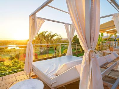 Lit de jour confortable avec rideaux sur terrasse avec vue sur paysage verdoyant au coucher du soleil.