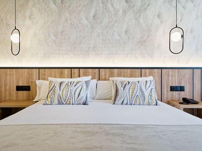 Chambre d'hôtel moderne avec grand lit, coussins décoratifs et tables de chevet en bois.