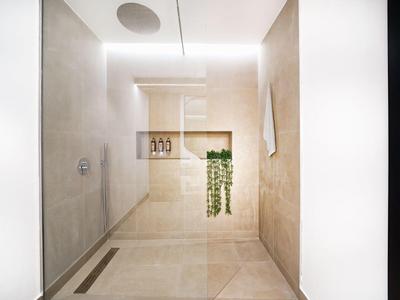 Douche à l'italienne moderne et minimaliste avec carrelage beige et étagères intégrées.