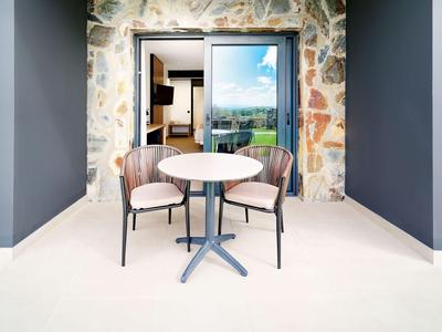 Balcone moderno con tavolo rotondo bianco e due sedie imbottite davanti a porta scorrevole in vetro.