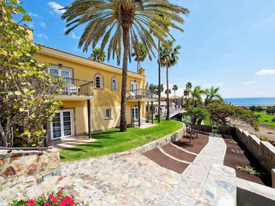 Hotel con edificio giallo, palme e sdraio sulla riva soleggiata con vista mare.