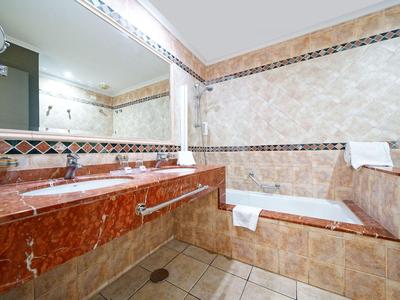 Bagno di lusso con piastrelle beige, pavimento in marmo rosso e vasca da bagno.