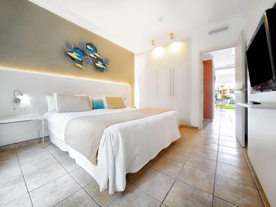 Camera d'hotel moderna con letto matrimoniale, mobili bianchi e accesso a una terrazza.