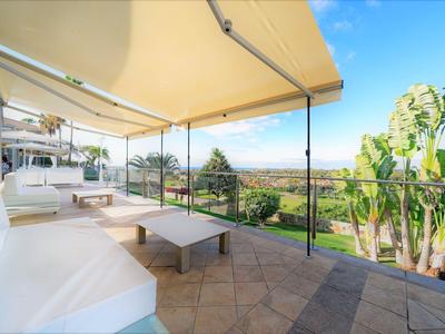 Terrazza con sedute bianche e vista su piante tropicali sotto un cielo azzurro.