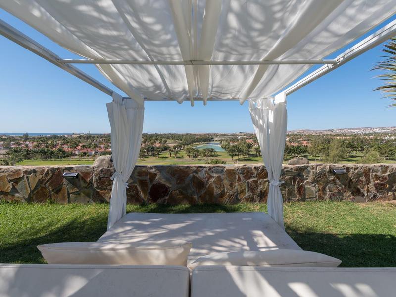 Coin salon ensoleillé sous un auvent blanc avec vue sur un paysage vert.