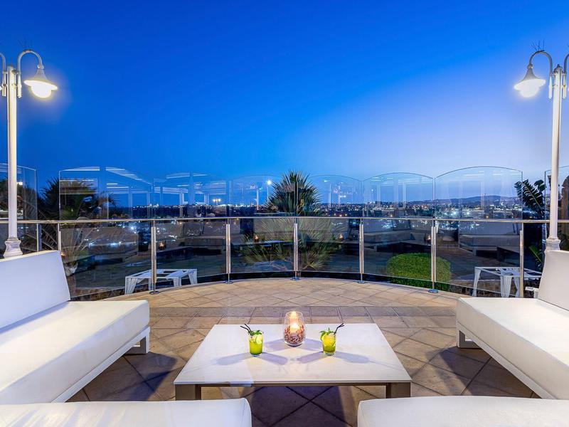 Espace extérieur confortable avec bancs blancs, table et lanternes la nuit.
