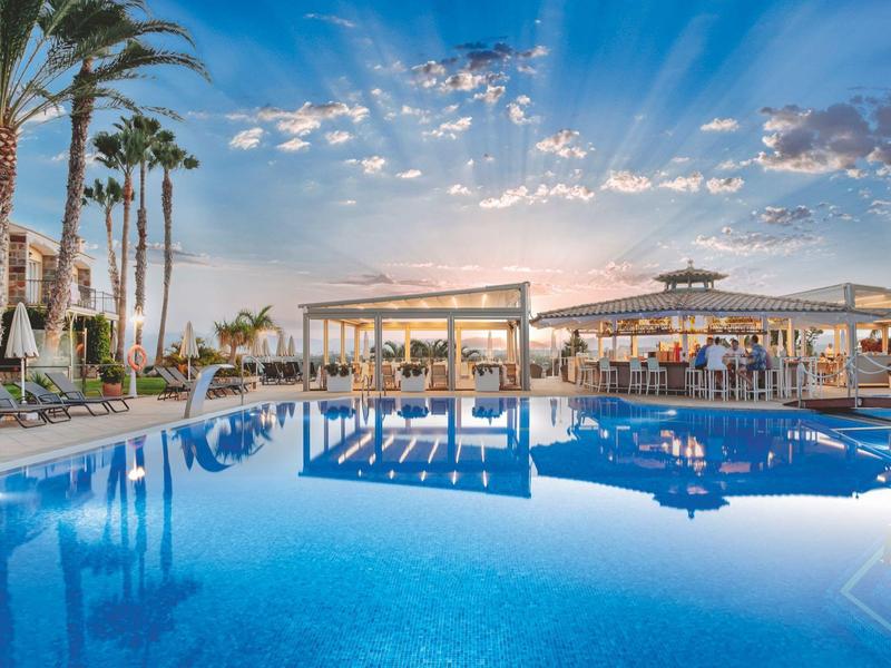 Grande piscine d'hôtel avec palmiers et espaces lounge confortables au coucher du soleil.
