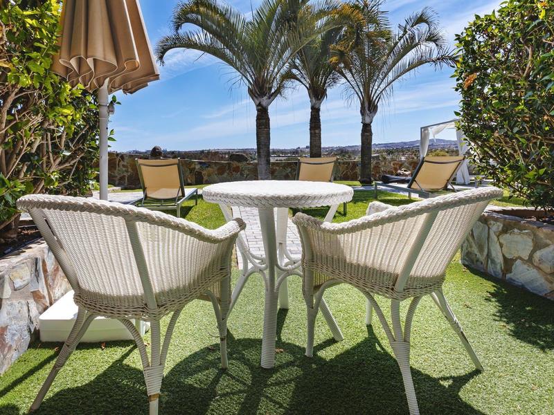 Coin salon confortable avec chaises et table sur terrasse avec vue sur la mer et les palmiers.