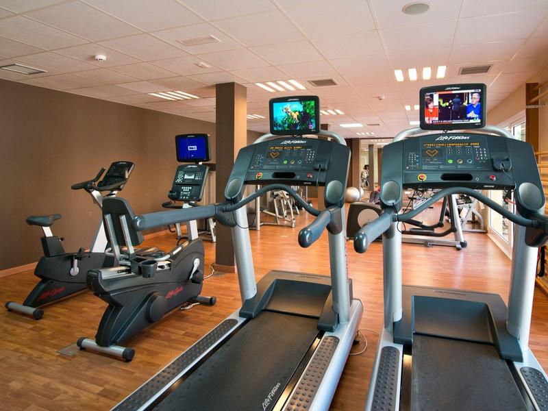 Salle de sport lumineuse avec tapis de course et vélos d'appartement sur sol en bois