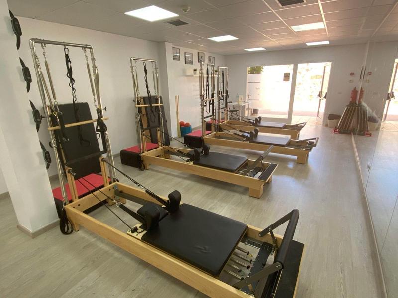 Salle lumineuse avec plusieurs reformeurs de Pilates en bois et miroirs au mur.