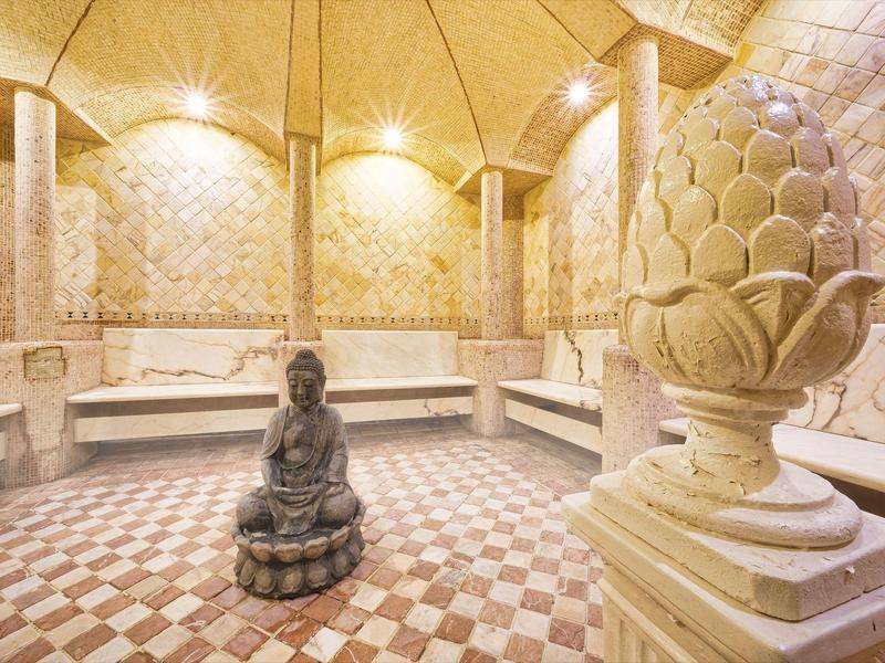 Une salle de spa luxueuse avec des carreaux de mosaïque, des statues en pierre et des murs illuminés.