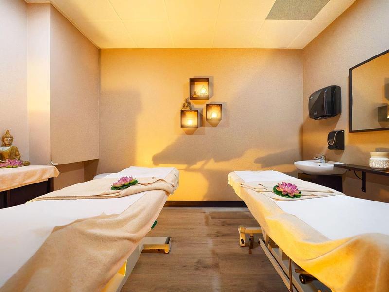 Salle de spa calme avec deux tables de massage, couleurs chaudes et éléments décoratifs.