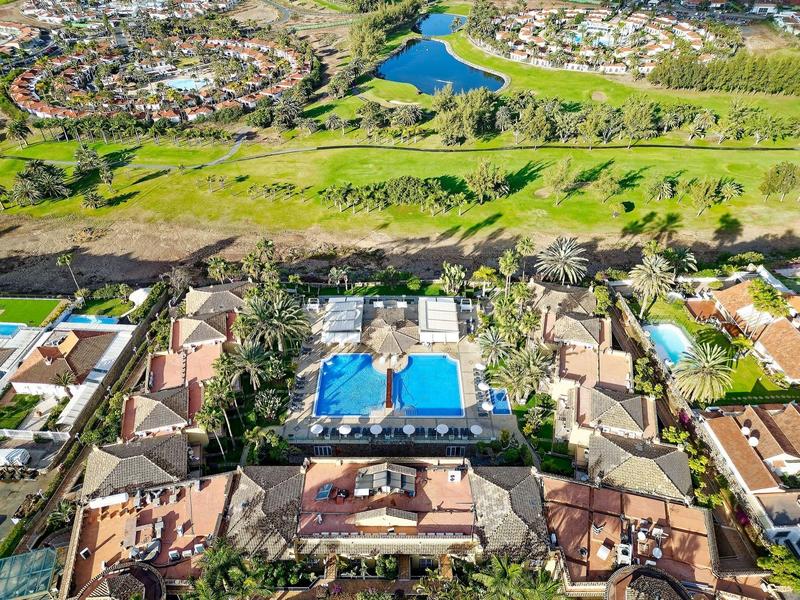 Vue aérienne d'un hôtel avec deux piscines bleues, entouré de verdure et de maisons résidentielles.