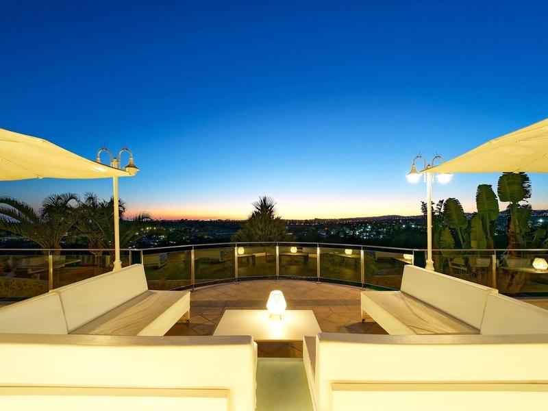 Vue d’une terrasse blanche moderne avec sièges et lampes au coucher du soleil.