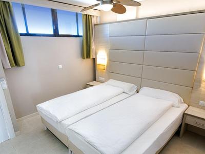 Chambre d'hôtel moderne avec deux lits simples, éclairage doux et fenêtres hautes.