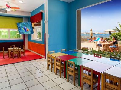 Salle colorée avec tables, chaises, vue sur plage et mer depuis la fenêtre.