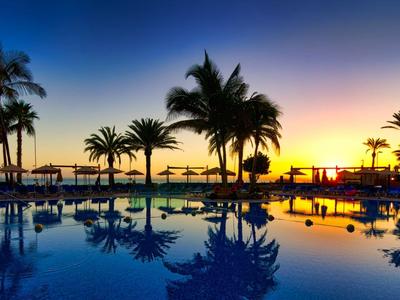 Pool und Palmen bei Sonnenuntergang an einem tropischen Urlaubsort