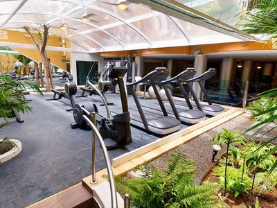 Moderner Fitnessraum mit Laufbändern und Kraftgeräten, umgeben von Pflanzen und natürlichem Licht.