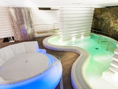 Spa moderne avec baignoire ronde et piscine aux formes organiques, éclairage coloré doux.