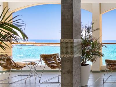 Terrasse d'hôtel avec fauteuils face à la mer turquoise sous un ciel bleu clair.