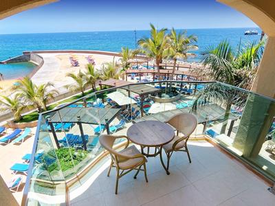 Balcon d'hôtel avec table et chaises donnant sur une plage sableuse et une mer bleue.