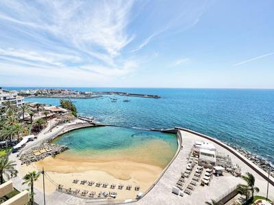 Vue aérienne d'une plage avec chaises longues et mer bleue sous un ciel partiellement nuageux.