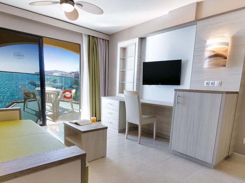 Chambre d'hôtel lumineuse avec vue sur mer, balcon, télévision, et mobilier moderne.