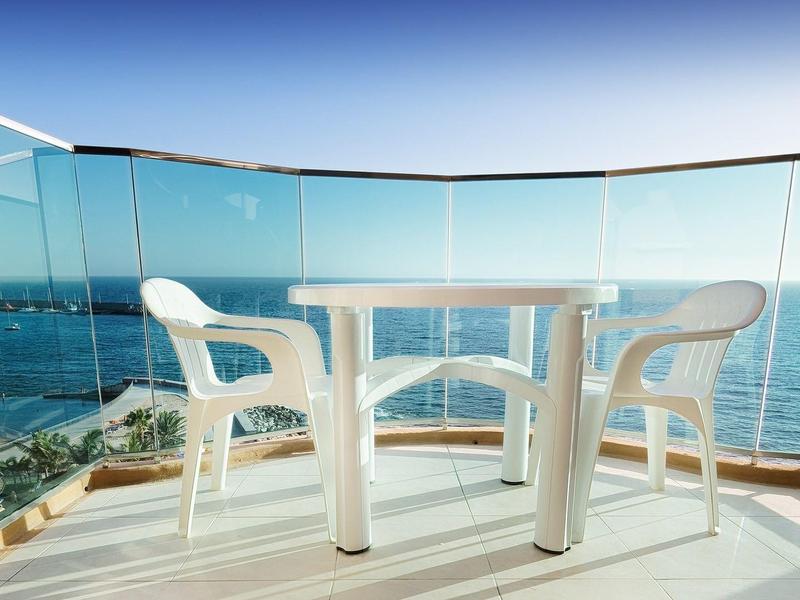 Balcon avec table et chaises blanches avec vue sur la mer et ciel bleu.