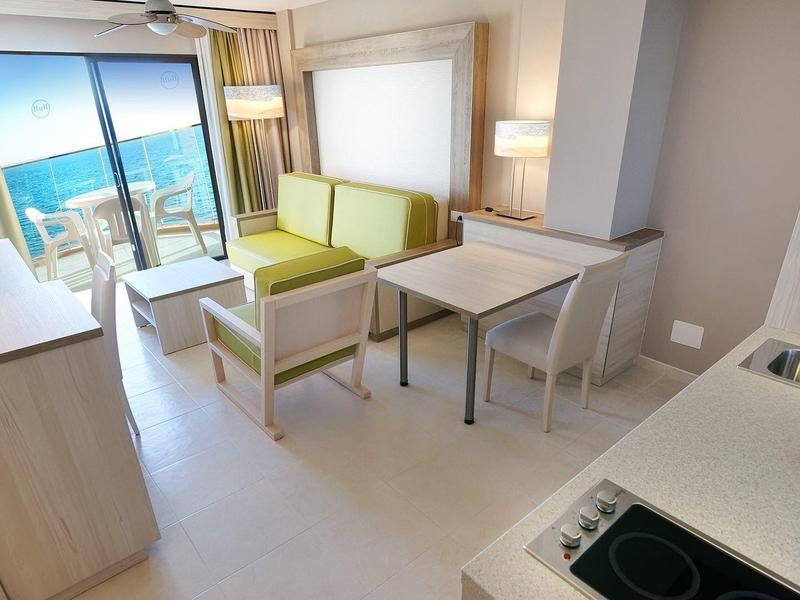 Séjour moderne avec canapé, table, cuisine intégrée et vue sur mer depuis la terrasse.