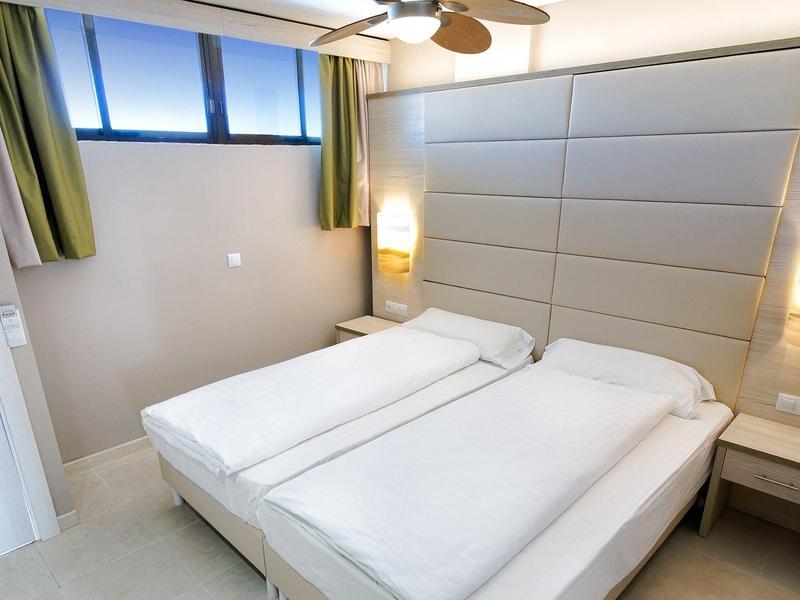 Chambre d'hôtel moderne avec deux lits simples, éclairage doux et fenêtres hautes.