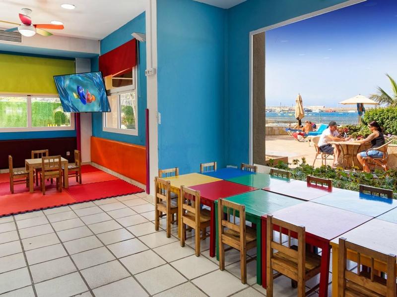 Salle colorée avec tables, chaises, vue sur plage et mer depuis la fenêtre.