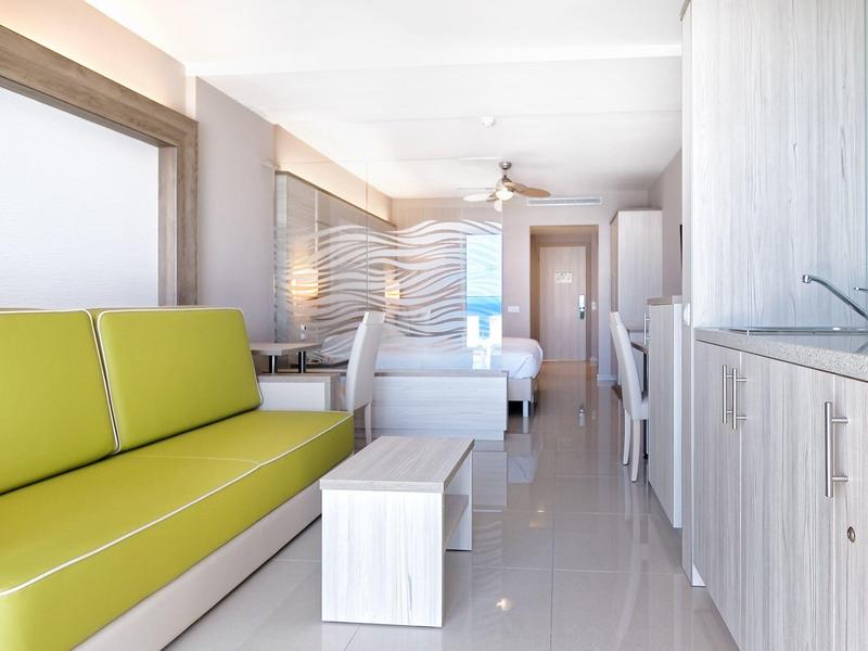 Intérieur moderne d'un appartement avec canapé vert, lit et kitchenette claire.