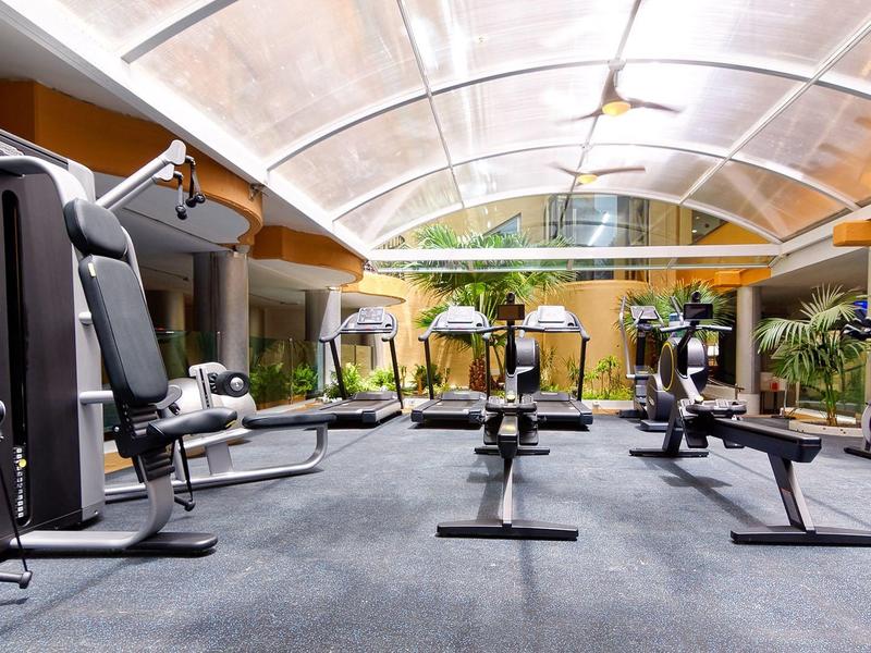 Salle de sport spacieuse avec machines modernes et toit en verre courbe.