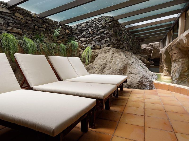 Chaises longues blanches alignées sous une verrière avec murs en pierre et sol carrelé.