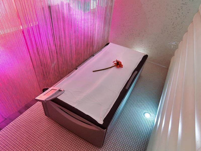 Lit de massage dans une cabine douce avec éclairage rose et rideaux blancs.