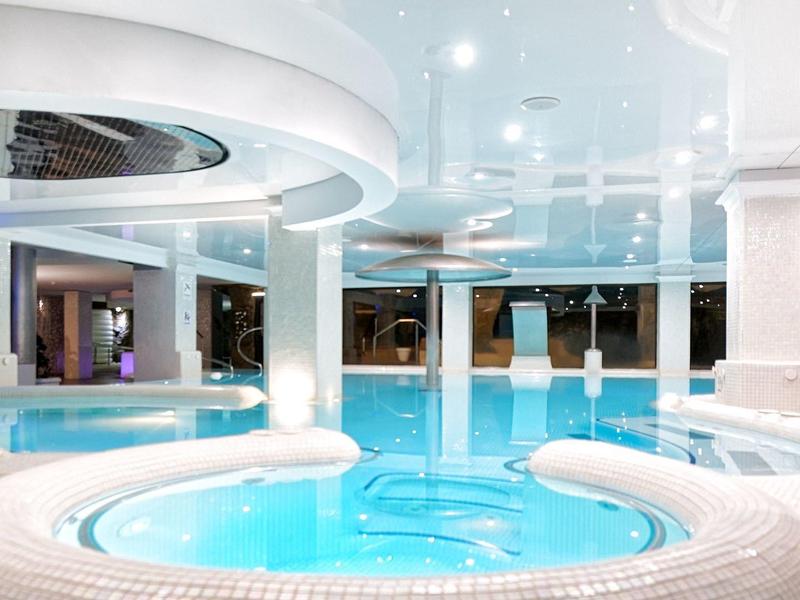 Piscine intérieure moderne avec éclairage doux et sièges intégrés, ambiance relaxante d'hôtel.
