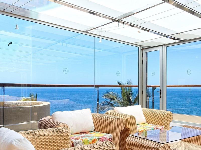 Terrasse d'hôtel confortable avec vue dégagée sur la mer et fauteuils en osier beige.