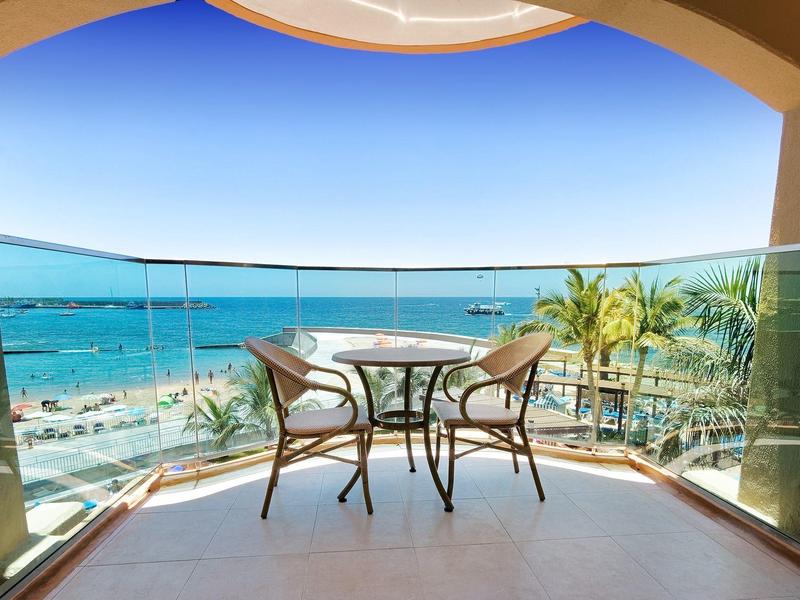 Balcon avec table et chaises, vue panoramique sur la mer et la plage ensoleillée.