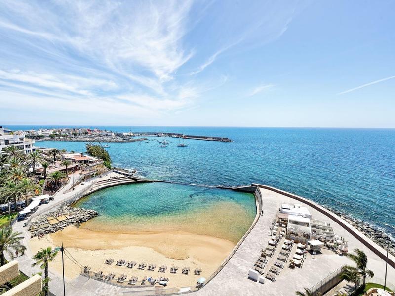 Vue aérienne d'une plage avec chaises longues et mer bleue sous un ciel partiellement nuageux.