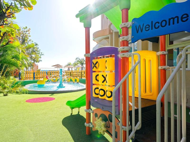 Aire de jeux colorée pour enfants avec toboggan et panneaux, sous un ciel ensoleillé.