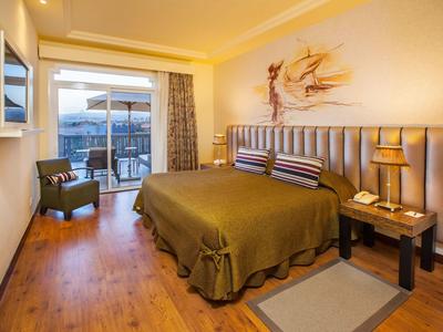 Modernes Hotelzimmer mit Doppelbett, Balkon, Sesseln und warmem Holzfußboden.