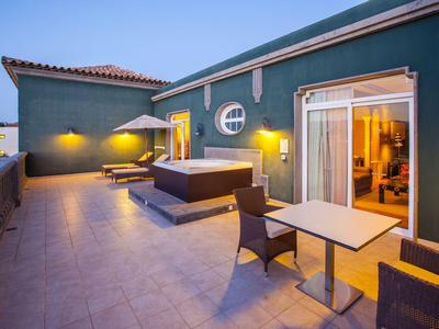 Moderner Hotelbalkon mit Sofas, Tisch und gelb beleuchtetem Innenraum bei Dämmerung.