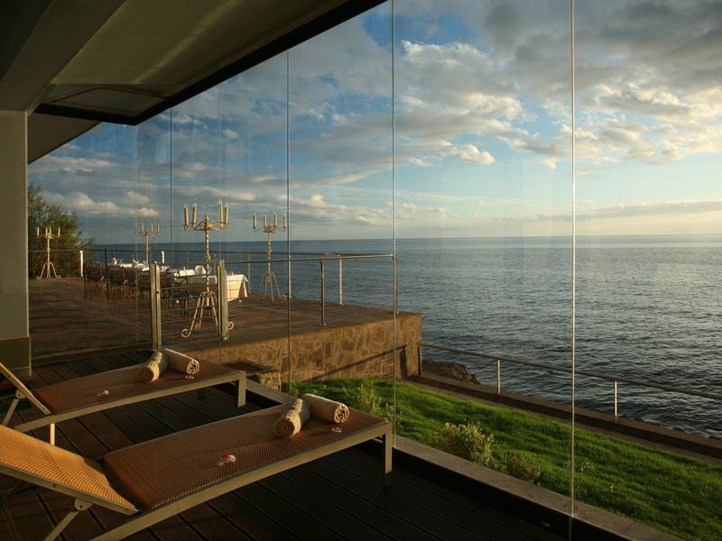 Vista al mar desde una terraza con tumbonas y barandilla de vidrio al atardecer.