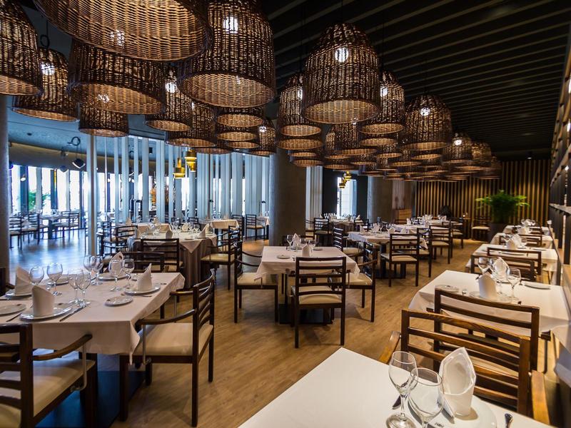 Restaurante elegante con mesas y sillas de madera y lámparas decorativas en el techo de madera.