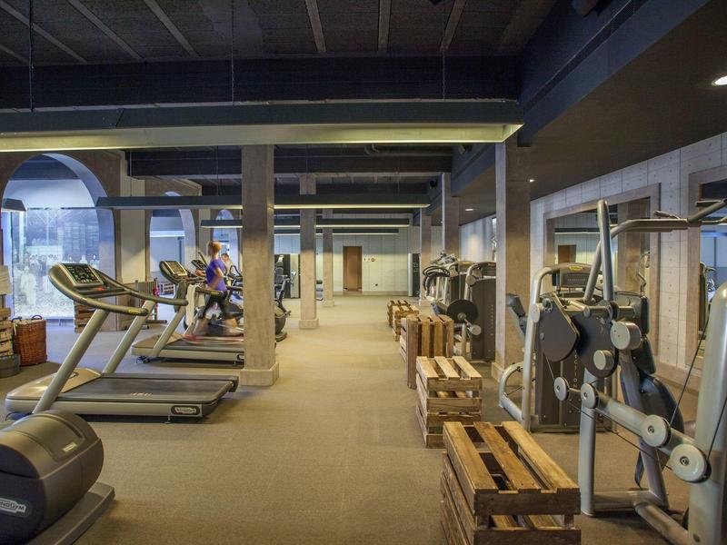 Gran gimnasio con cintas de correr, pesas y bancos de madera en un hotel.
