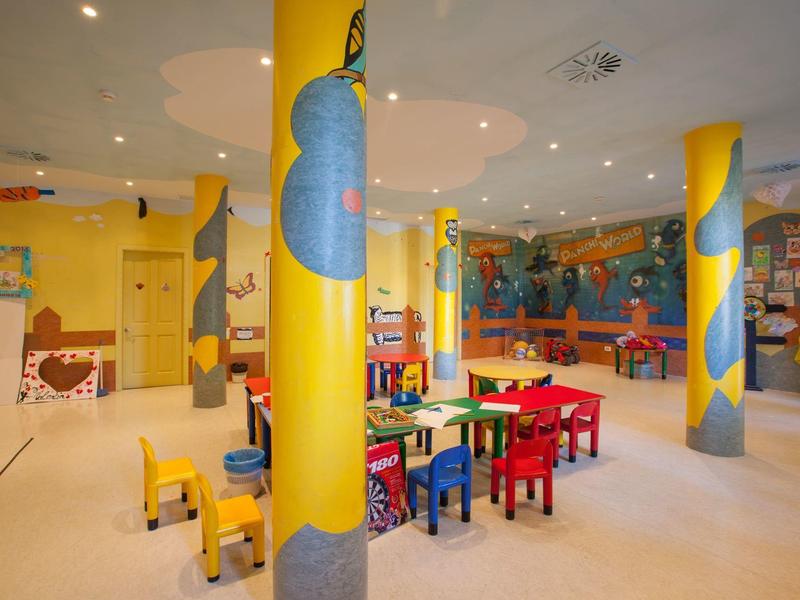 Sala de juegos infantil colorida con mesas, sillas y columnas pintadas en un hotel.