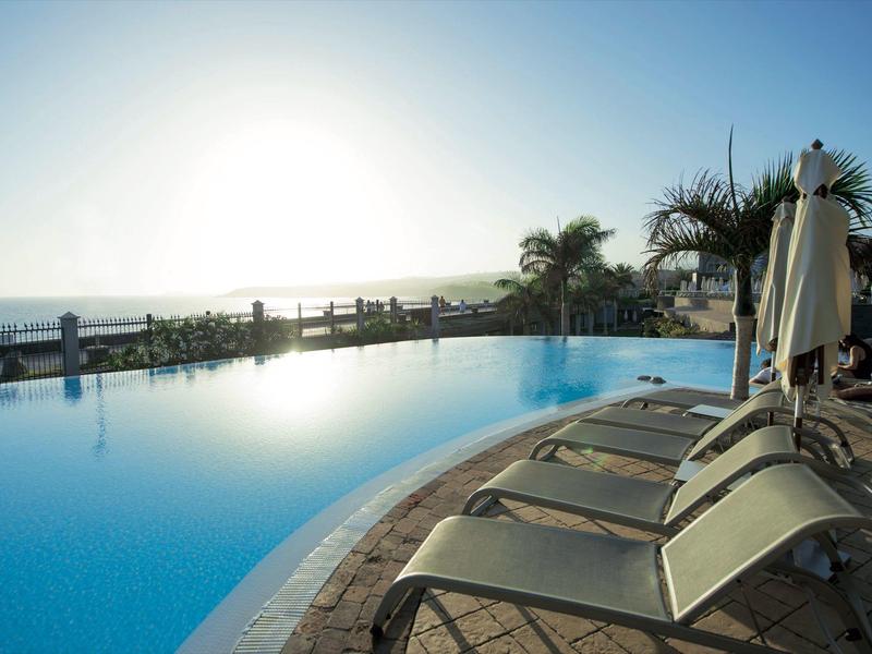 Piscina infinita con tumbonas y vista al océano al atardecer.